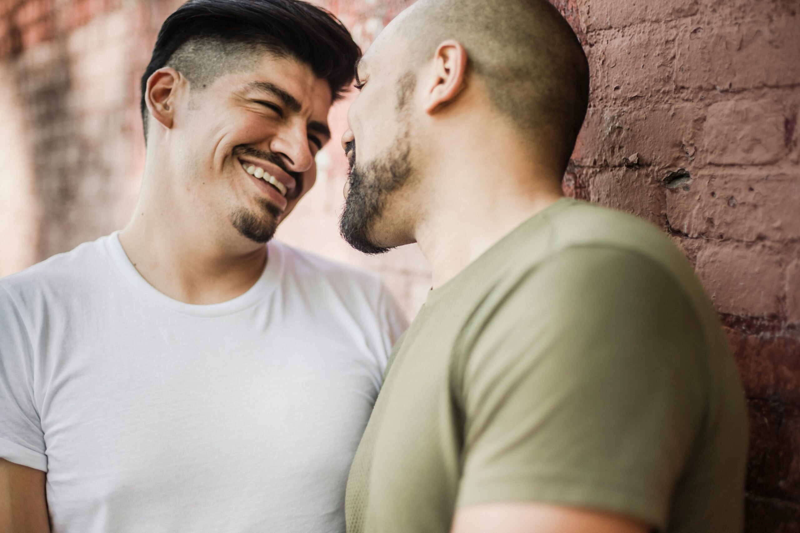Happy LGBTQ+ couple sharing a tender moment by a brick wall. Love and laughter in urban setting.